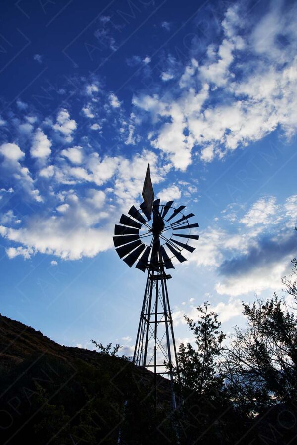 windmill silhouette against a blue sky with fluffy clouds